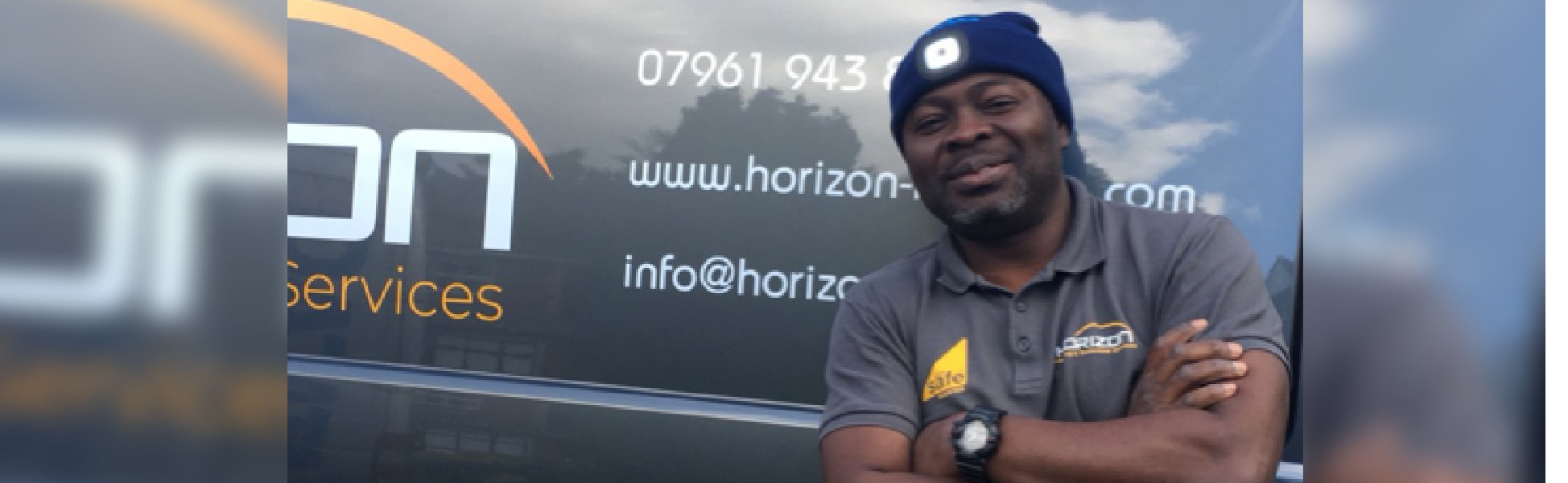 A man wearing a blue hat stands in front of a parked van, showcasing a casual outdoor scene.